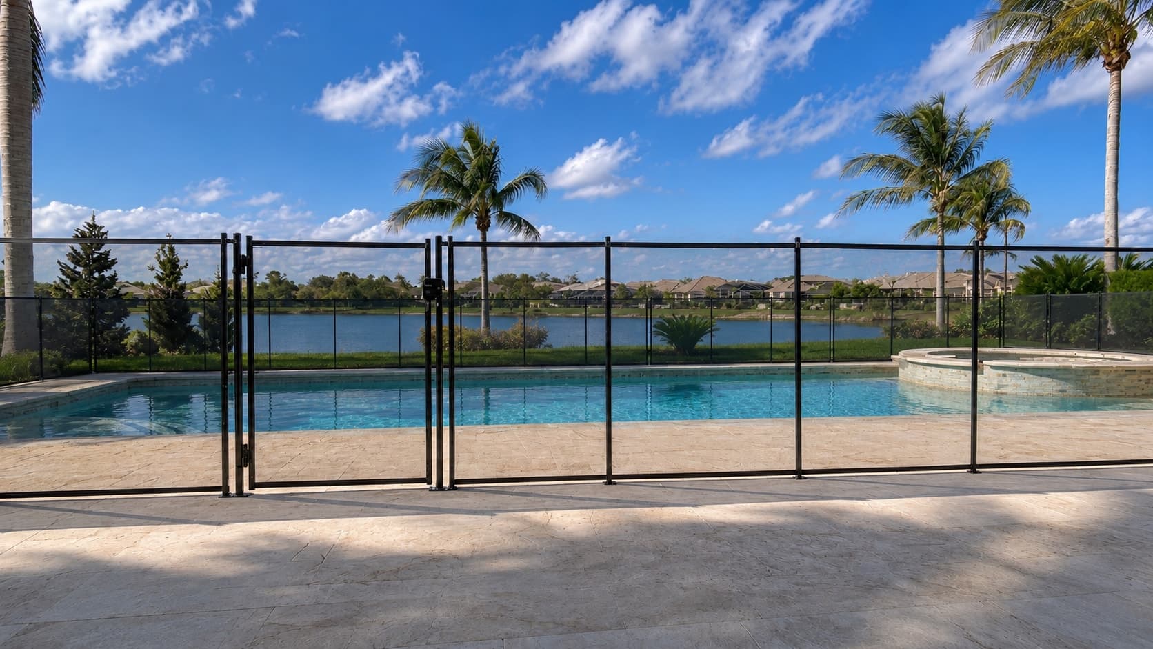 Backyard pool by a lake enclosed by a tall black mesh safety fence