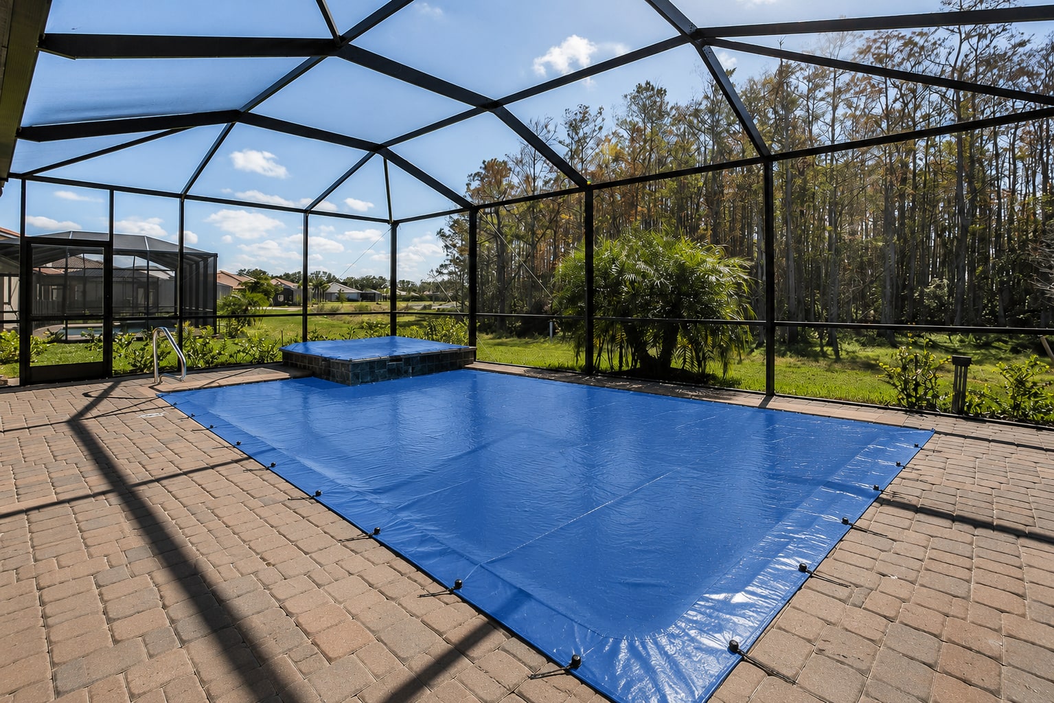 Pineapool walk-on safety cover installed on a screened Florida lanai pool with a spa, backing onto a wooded lot